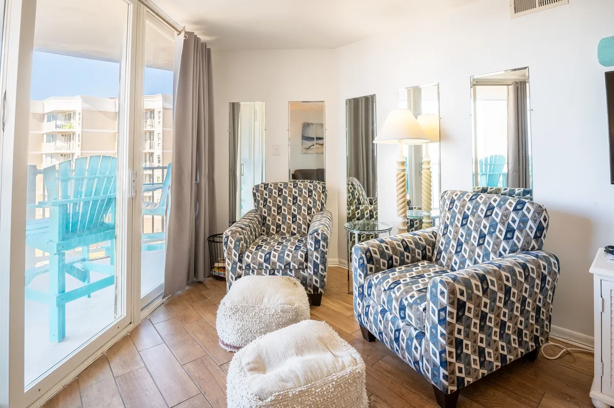 A cozy seating area featuring blue patterned armchairs and light-colored ottomans, with large mirrors on the wall and a window that offers a glimpse of the outside. The space feels bright and welcoming, suggesting a relaxing spot to unwind after a day of island adventures.