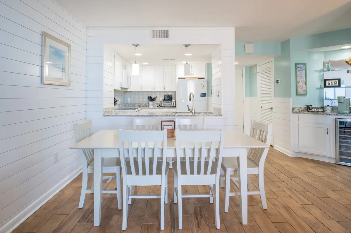 A bright, welcoming view of the dining table and kitchen island, with modern light fixtures overhead. The table is perfectly situated for family meals or casual breakfasts, with the kitchen just steps away, illustrating the open-concept layout.