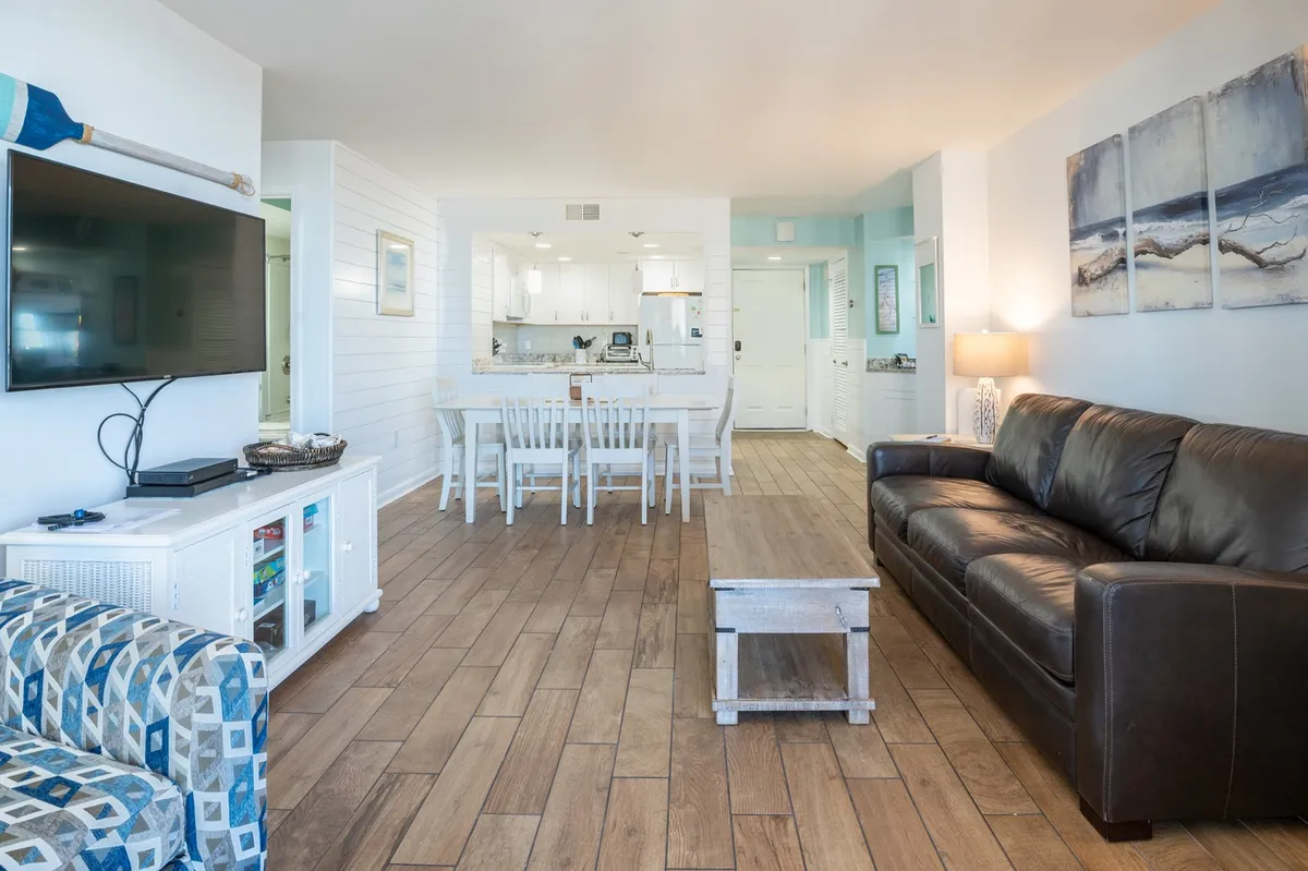A cozy living room with a leather sofa, dining table, and entertainment area, all bathed in comfortable lighting. The scene suggests a versatile space for relaxing, socializing, or planning outings.