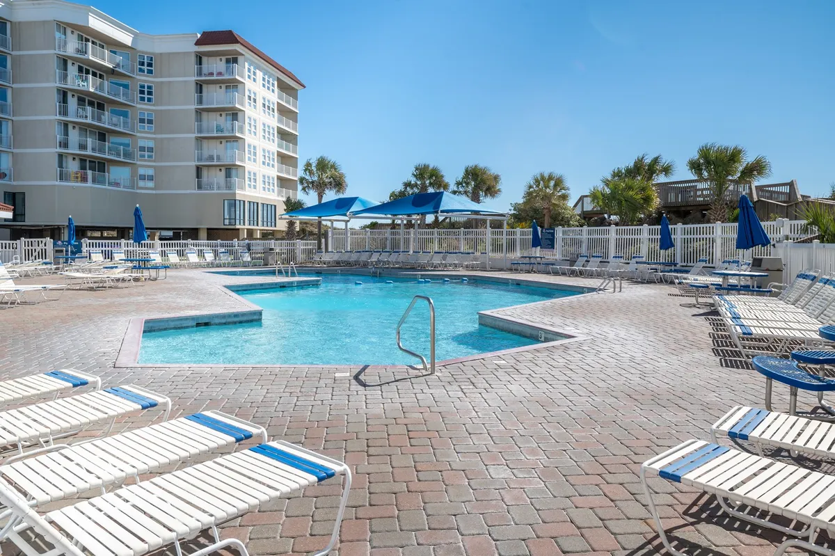 This image displays a vibrant outdoor swimming pool area at the resort, complete with lounge chairs, umbrellas, and the building facade in the background. The pool is inviting and clearly suited for families, with plenty of space for swimming, sunbathing, and socializing by the water.