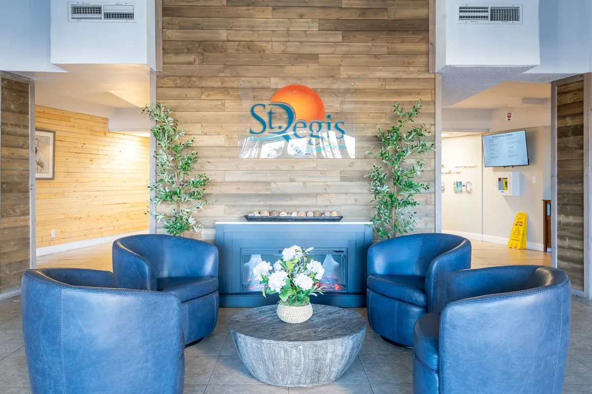 A welcoming lobby area with blue armchairs, a wooden accent wall, a fireplace, and a property logo on the wall. Fresh flowers on the center table add a touch of local charm, making this space feel like the gateway to your island adventure.