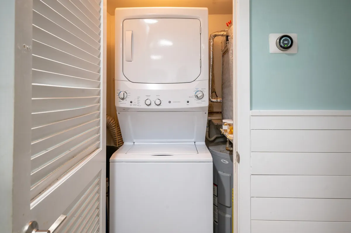 A practical view of an in-unit stacked washer and dryer, along with nearby utility controls. The simple setup reinforces the ease of handling laundry on-site, helping guests pack light and manage their own routines.
