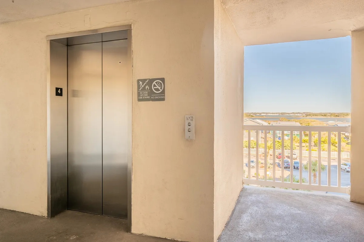 A calm corridor ending in an open doorway, through which daylight streams in. The scene includes an elevator and hints at the excitement of stepping out to a beautiful outdoor view, representing the transition from inside comfort to outside adventure.