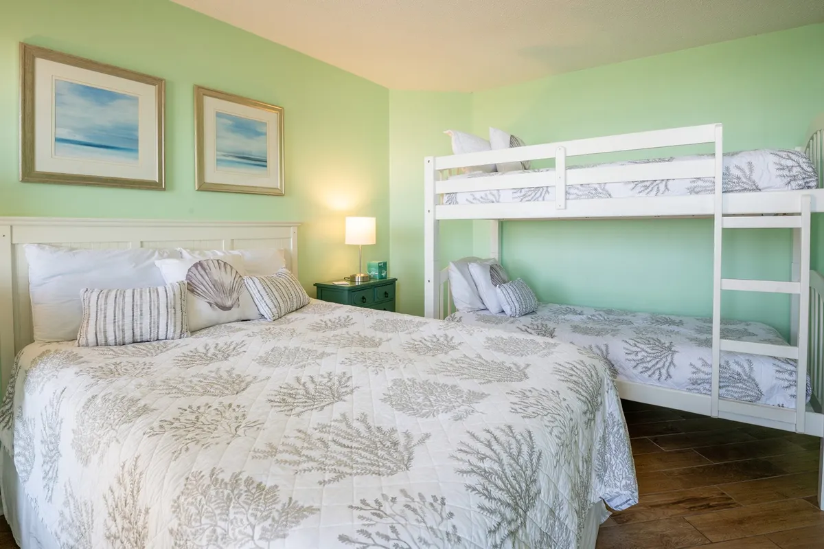 A comfortable guest bedroom featuring a queen-sized bed, twin-over-twin bunk beds, and framed artwork, all in a cozy, family-friendly atmosphere. The layout is perfect for families or groups, and the decor is both welcoming and functional.