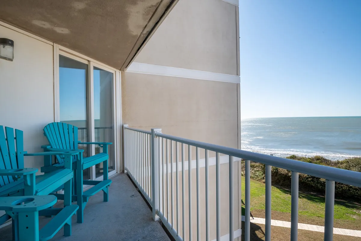 A serene private balcony with turquoise Adirondack chairs overlooking the ocean, accented by railings and a panoramic water view. The scene suggests tranquil moments of coffee at sunrise or unwinding at sunset as described in the section.